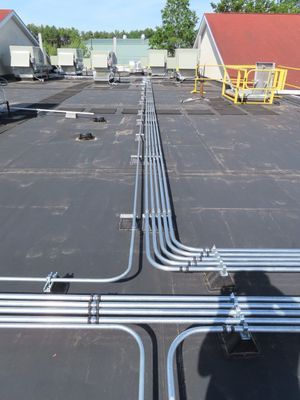 Parallel electrical conduits running across a flat black rooftop.