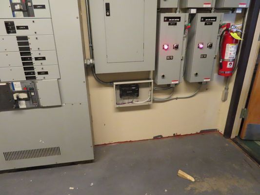 Electrical room wall with mounted control boxes and a fire extinguisher.