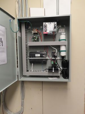 An open grey electrical control cabinet showing internal circuit components, including a digital controller and neatly organized wiring.