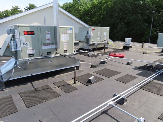 A rooftop installation featuring two Trane commercial HVAC units and metal conduits secured to the roof surface.