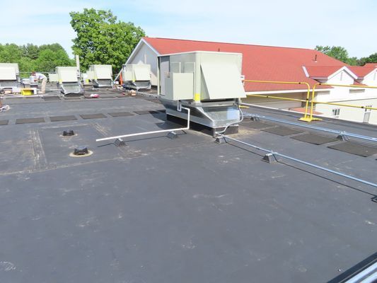 Several white rooftop HVAC units installed on a black flat roof with yellow safety guardrails in the background.