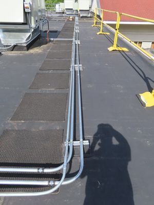 A long-distance shot of parallel electrical conduits and protective walkway mats leading across a commercial rooftop.