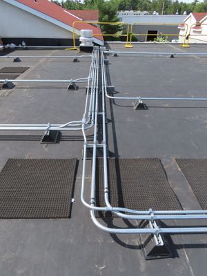 Close-up of multiple silver electrical conduits precisely installed and running across a black flat roof surface.