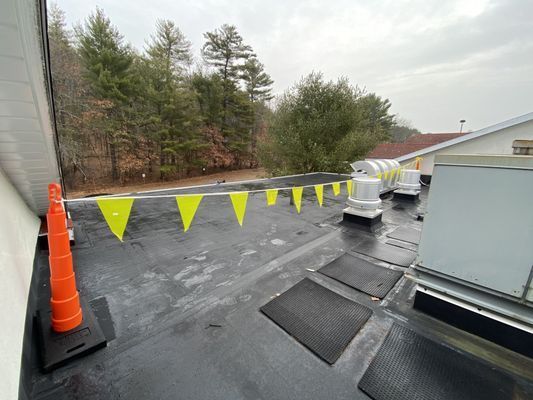 A row of yellow safety flags positioned along the perimeter of a black rooftop during a maintenance project.