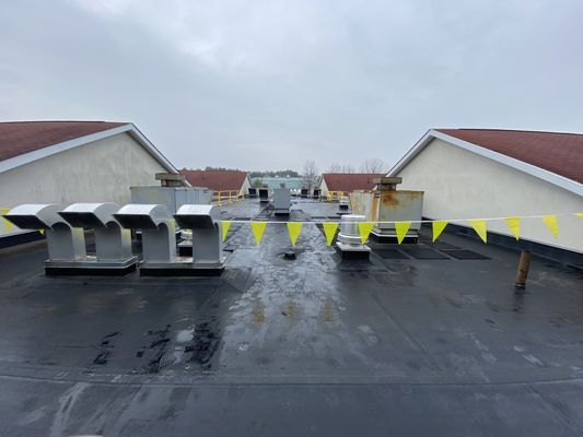 Rooftop mechanical equipment and vents on a flat roof, delineated by yellow safety flags near a building expansion.