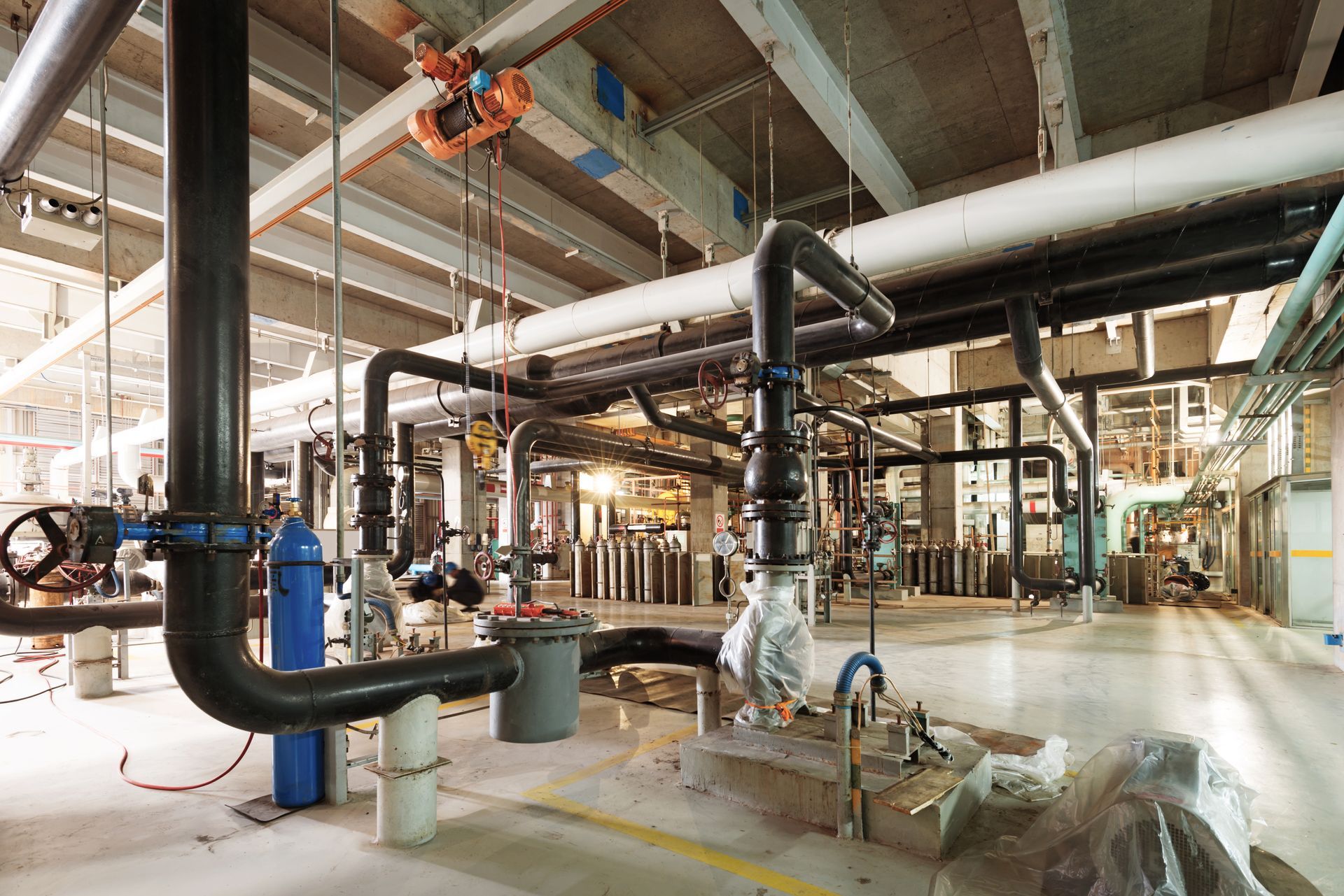 Wide shot of a network of heavy-duty black industrial pipes, valves, and a large grey filter unit in an open warehouse setting.