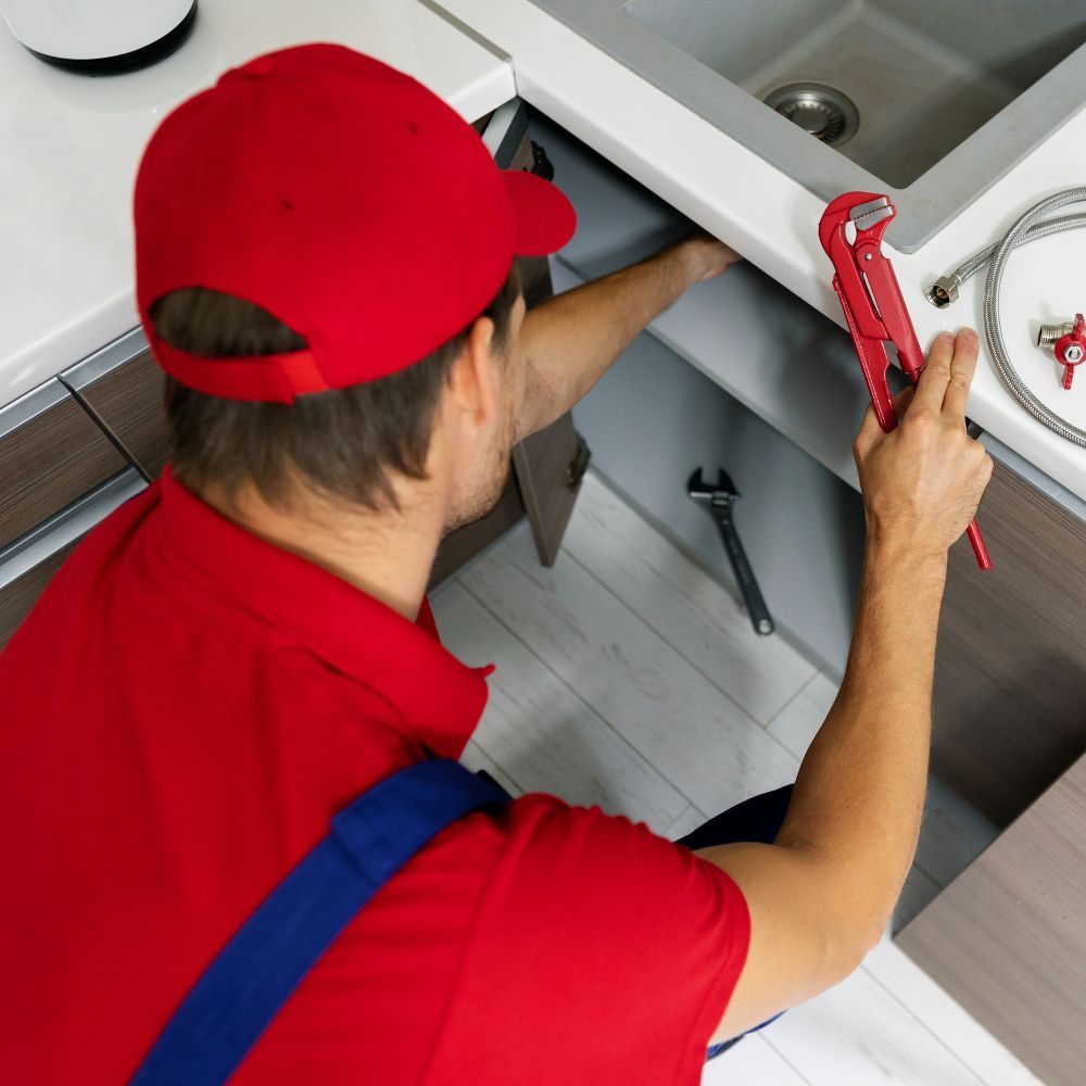 Plumber in a red uniform using a pipe wrench to work on a sink installation.