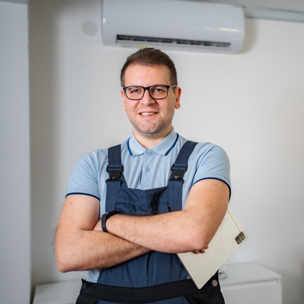 A friendly male technician in glasses and navy blue overalls posing with his arms crossed in a professional setting.