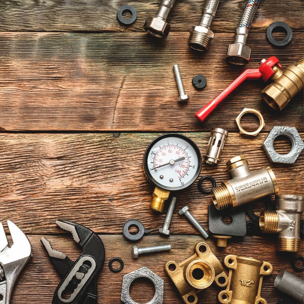 Flat lay of plumbing components including a pressure gauge, brass valves, and wrenches on a rustic wood background.