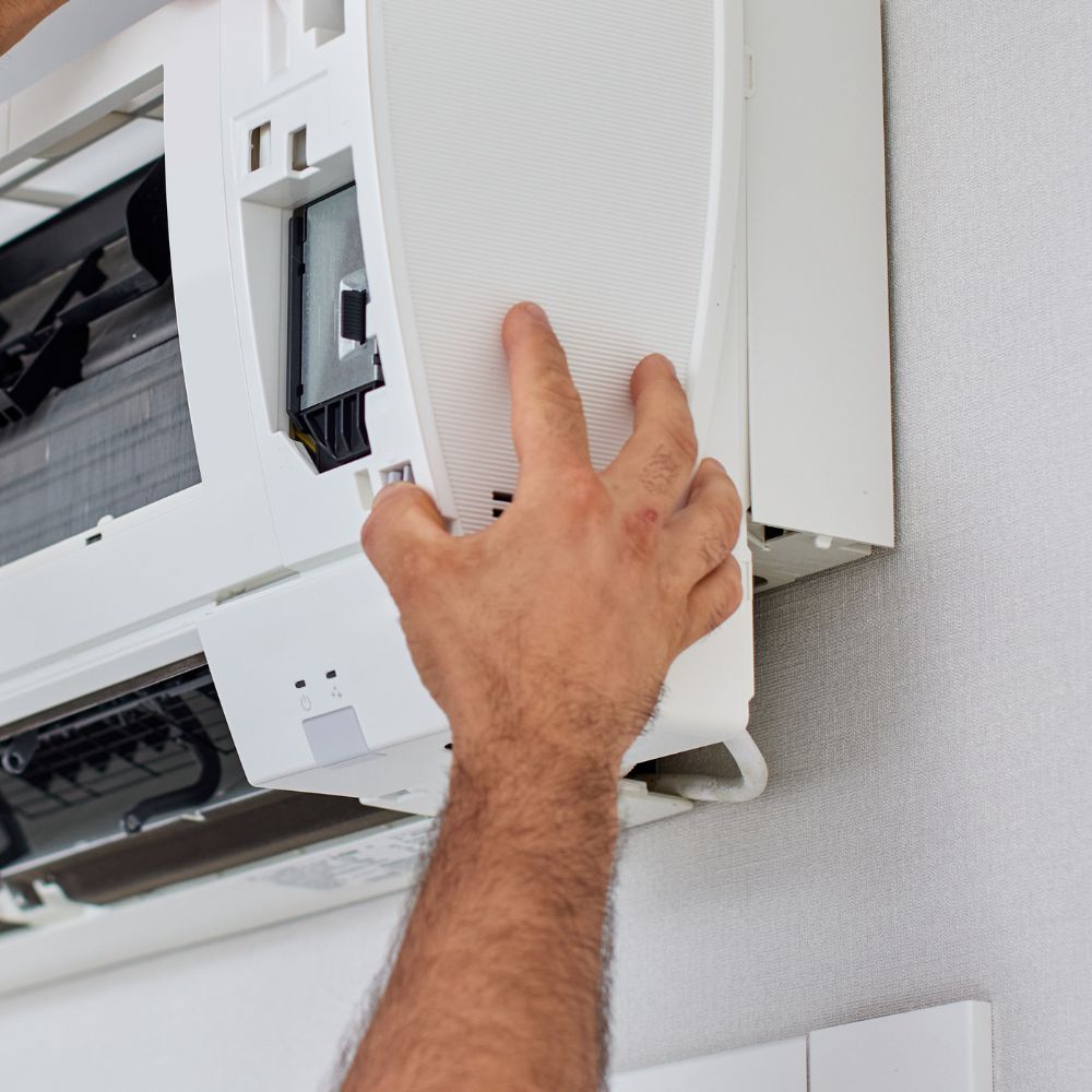 Close-up of a hand opening the front panel of an indoor air conditioner for inspection.