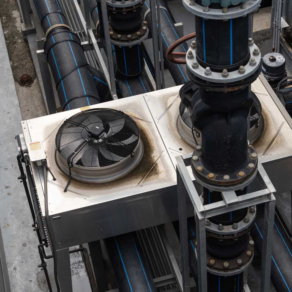 An overhead view of a commercial air conditioning unit with dual fans, connected to large black industrial pipes and valves.