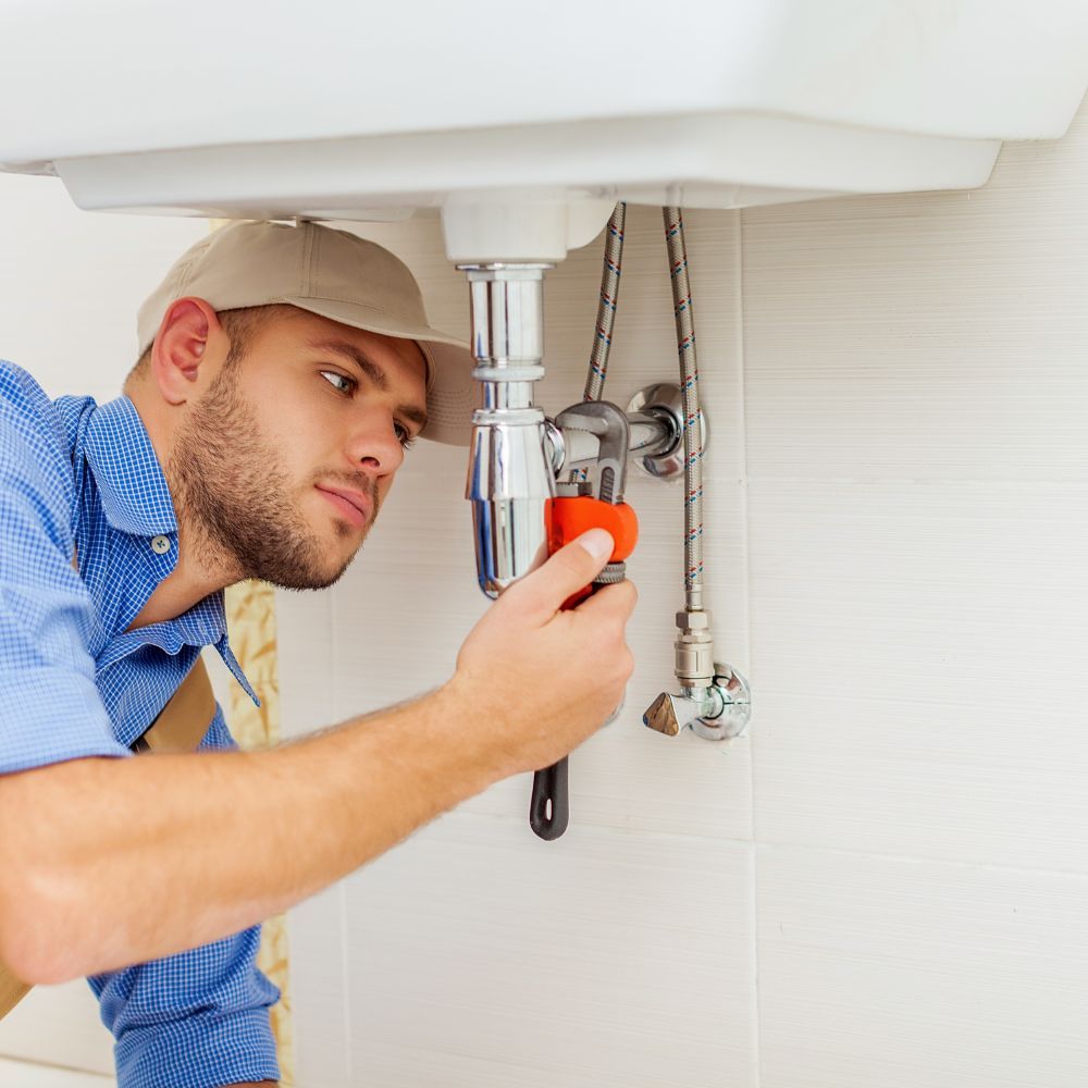 Plumber using a wrench to tighten a chrome P-trap under a bathroom sink.