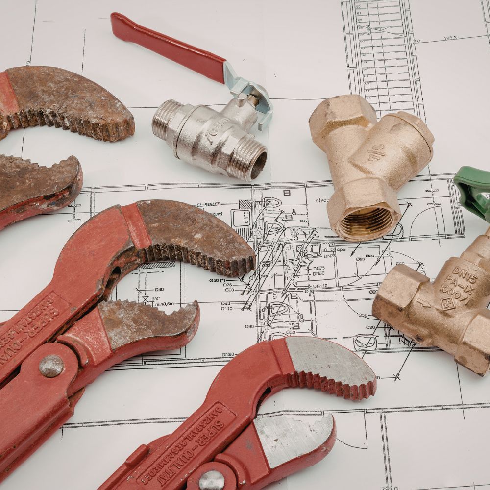 Assorted heavy-duty pipe wrenches and brass gate valves sitting atop a technical plumbing blueprint.
