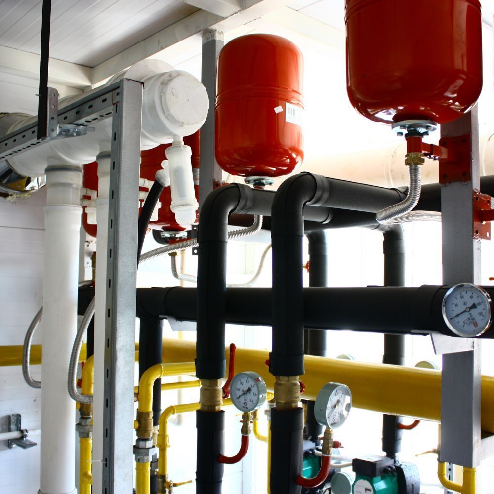 Industrial boiler room piping with insulated lines, red expansion tanks, and temperature monitoring gauges.