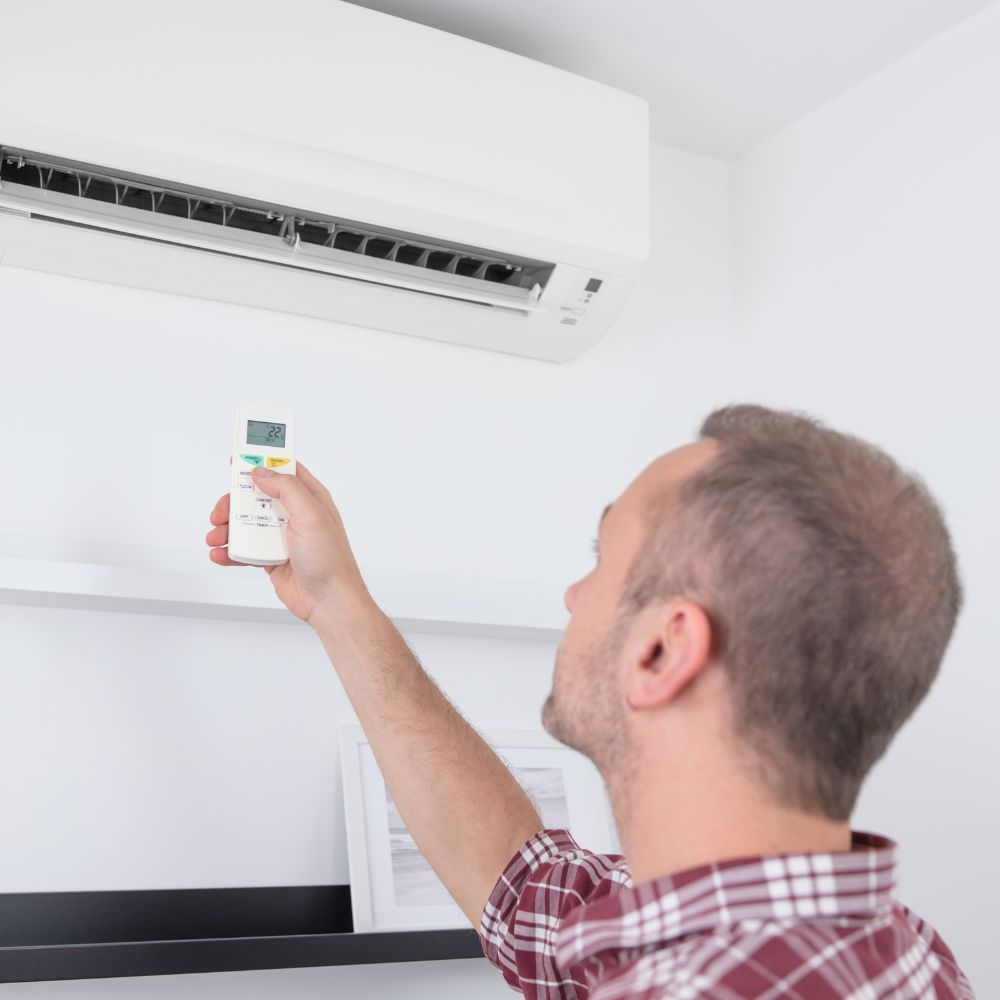 A man using a remote control to test or program a newly installed split-system AC unit.
