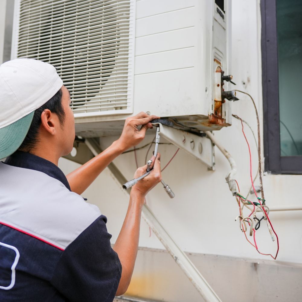 Professional HVAC technician repairing external wiring and components on an outdoor condenser unit.