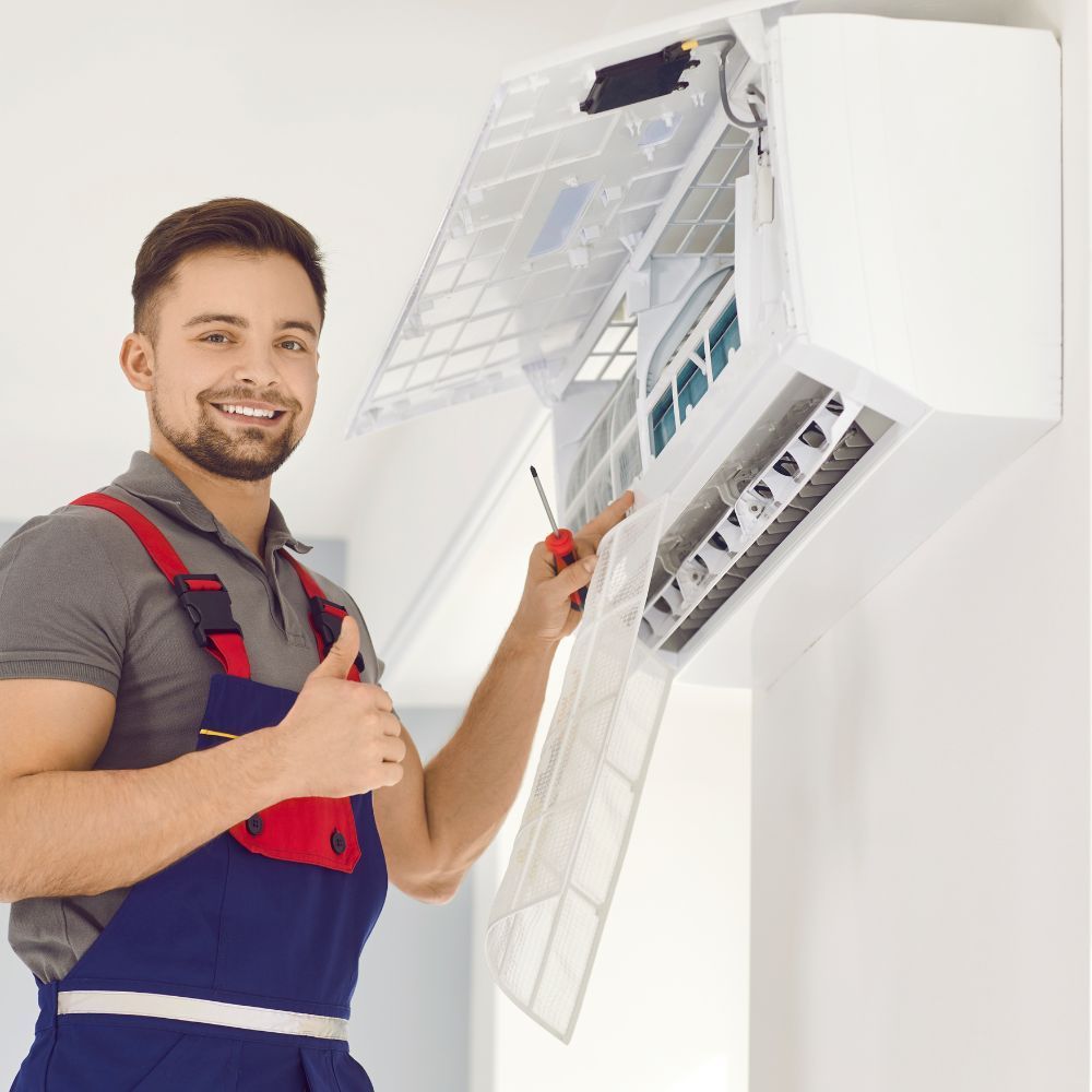 Friendly technician giving a thumbs up while inspecting an indoor ductless mini-split air handler.
