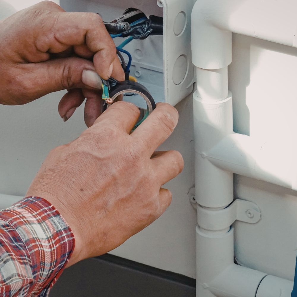 Close-up of a technician's hands applying electrical tape to wire connections inside a control box.