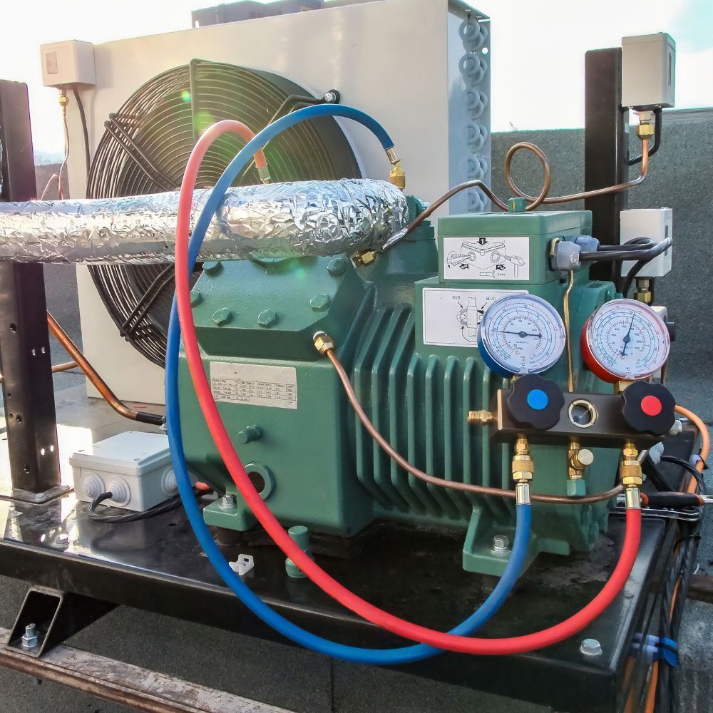 Industrial refrigeration compressor with dual pressure gauges and refrigerant charging hoses.