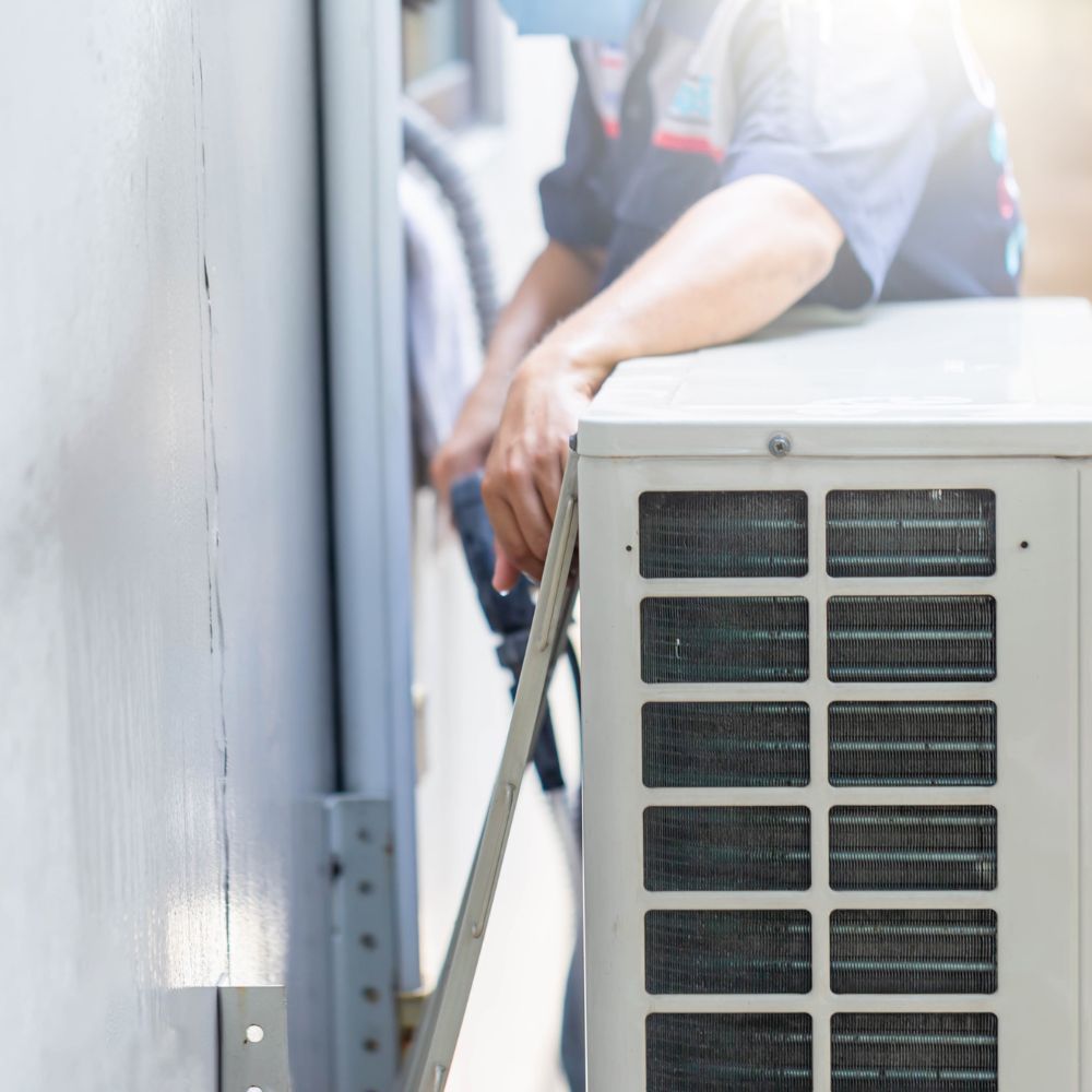 Technician performing a seasonal maintenance check on an outdoor HVAC condenser unit.