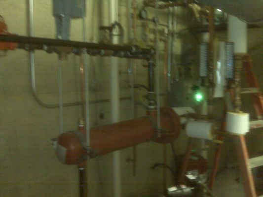 An orange horizontal pressurized tank and associated piping assembly inside a mechanical room.