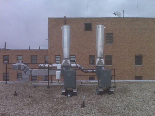 Wide shot of the rooftop equipment and exhaust stacks beside a multi-story brick building.