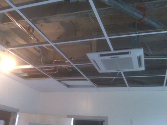A dropped ceiling grid showing an installed square white AC cassette vent and exposed metal ductwork.