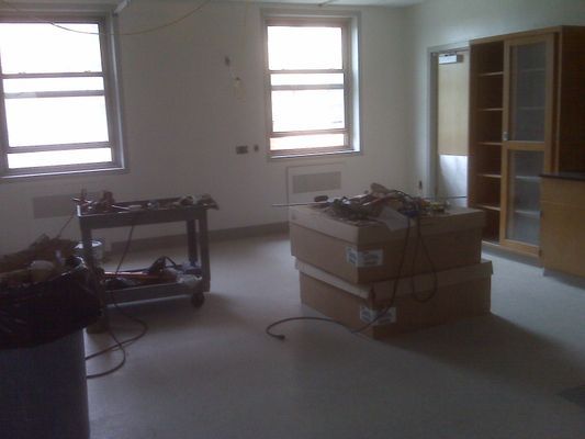 A room under renovation showing stacked boxes and tools on a workbench near bright windows.