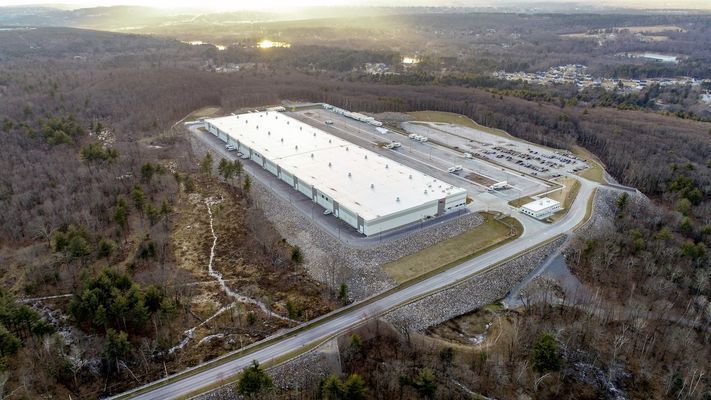 A high-angle wide shot of the industrial warehouse complex, showing its scale and surrounding landscape.