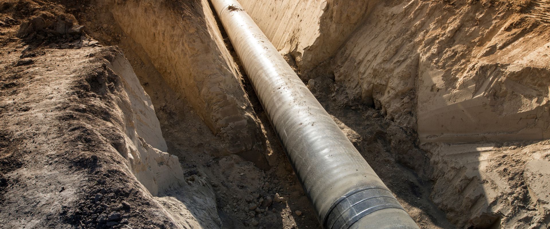 A massive industrial pipeline resting deep within a sandy excavation trench during an underground installation project.
