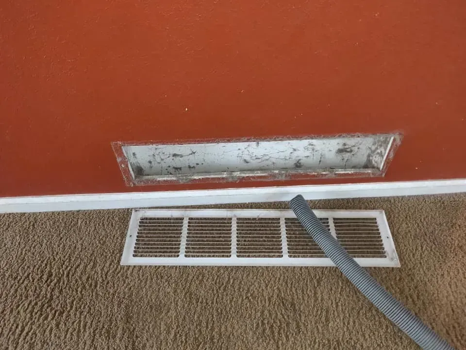 A vacuum cleaner is being used to clean a vent on the floor.