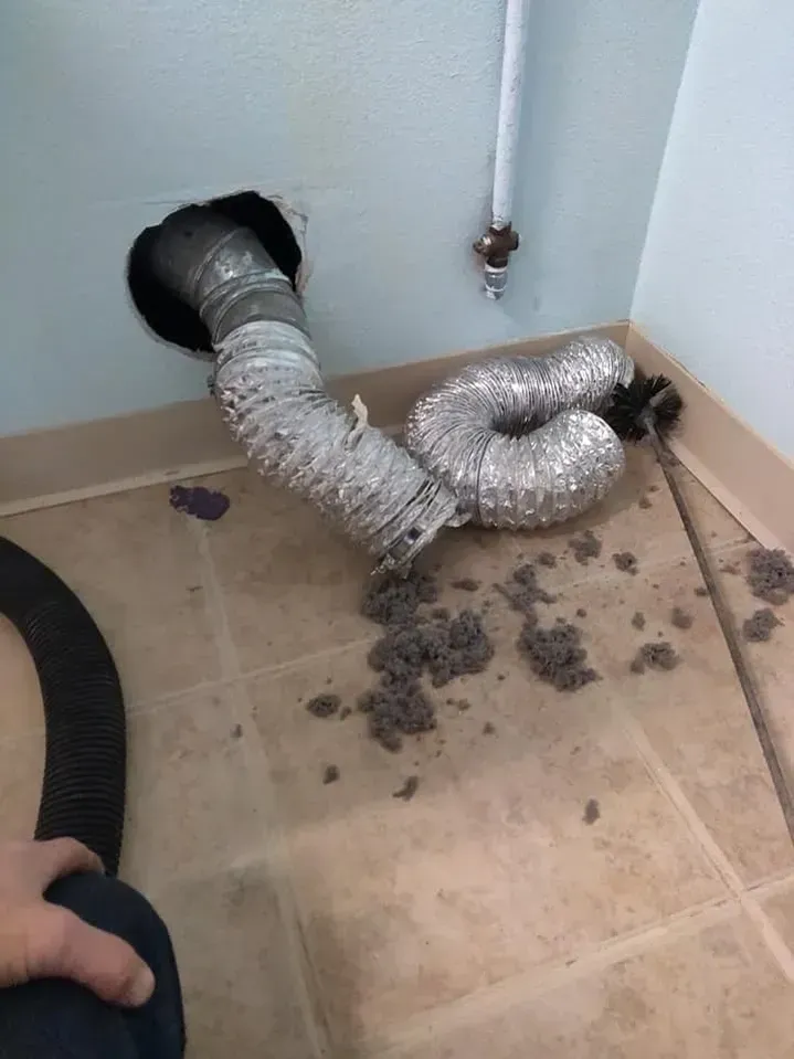 A person is cleaning a dryer vent with a vacuum cleaner.