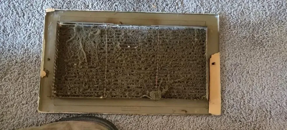 A dirty air vent is sitting on top of a carpet.