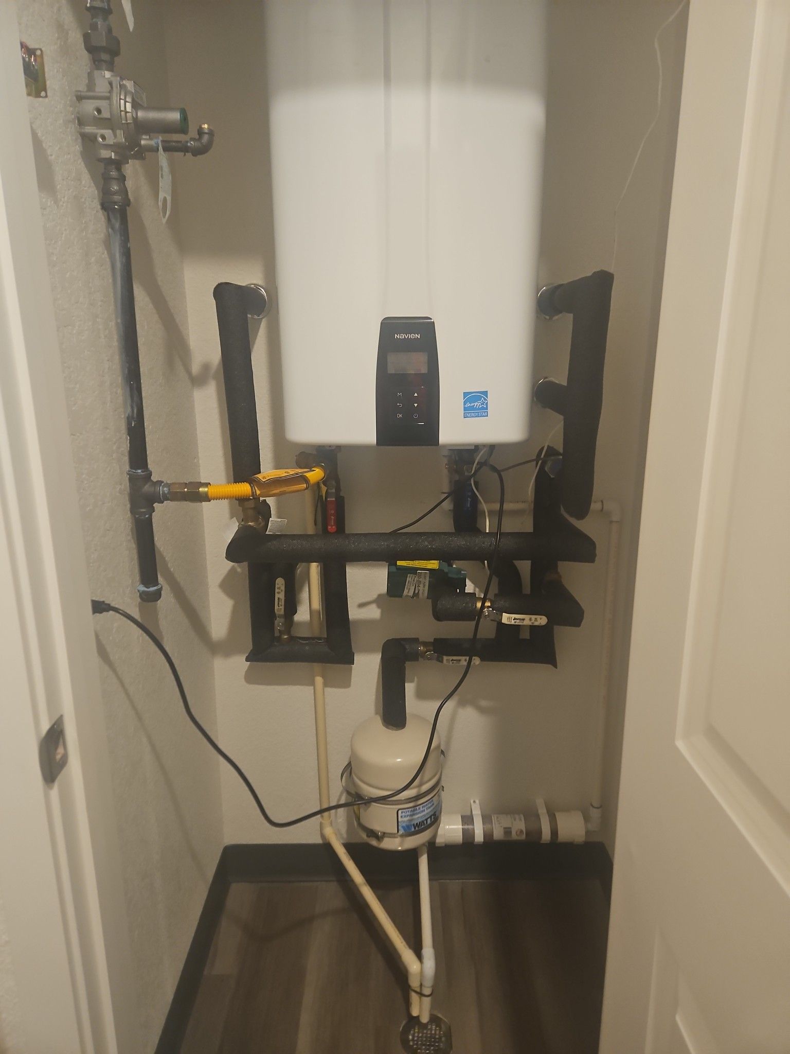 A white water heater is mounted to the wall in a bathroom.