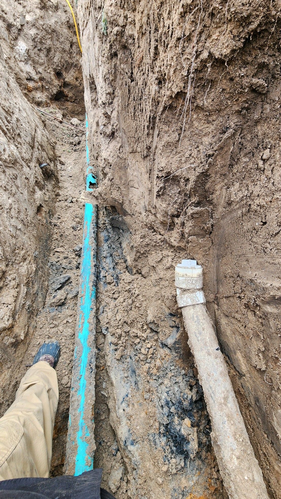 A person is standing in a trench next to a blue pipe.