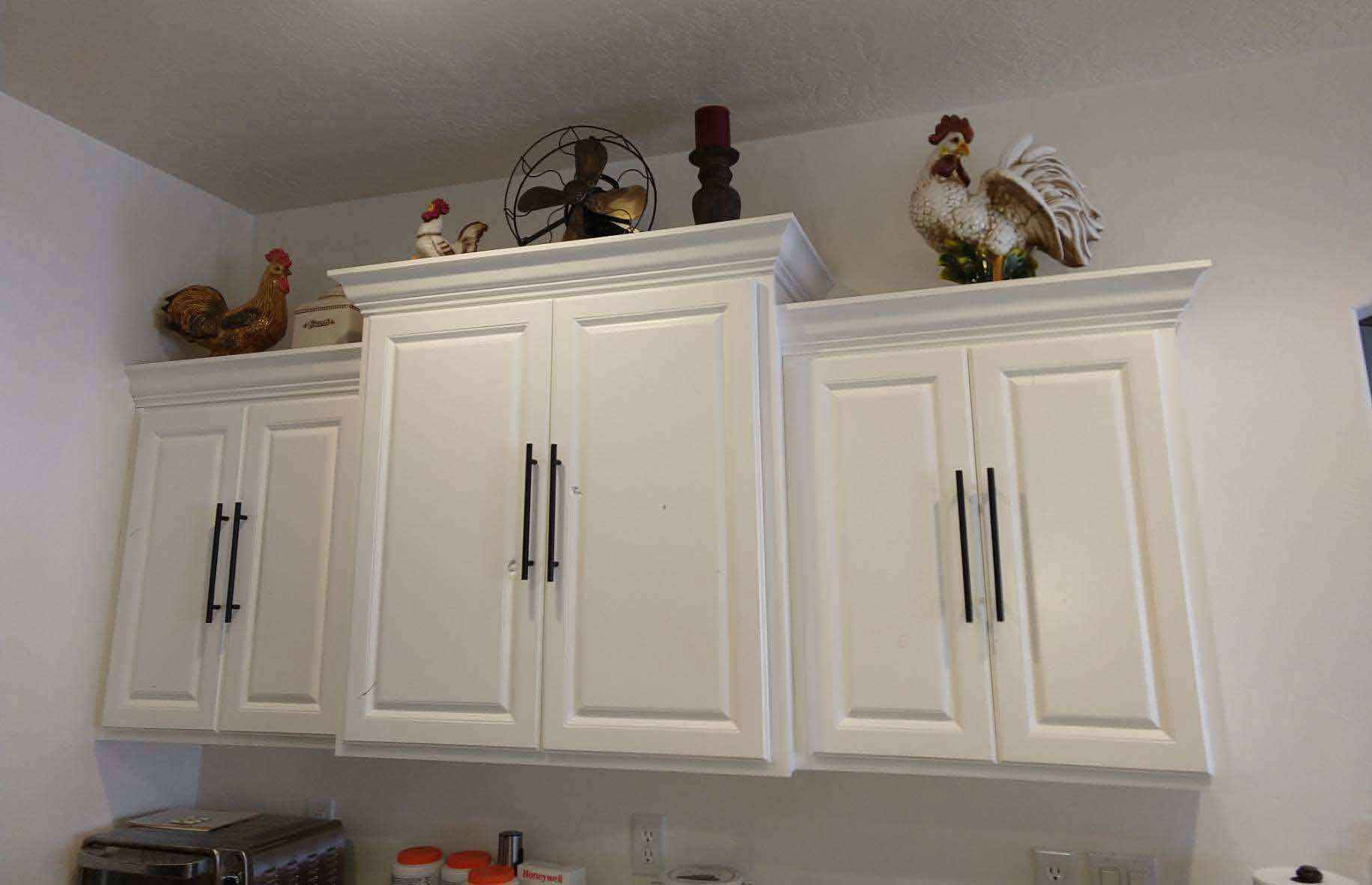 A kitchen with white cabinets and a fan on top of them.