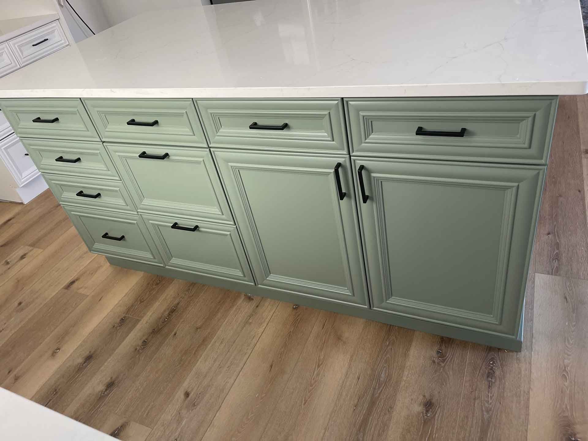 A kitchen island with green cabinets and drawers and a white counter top.