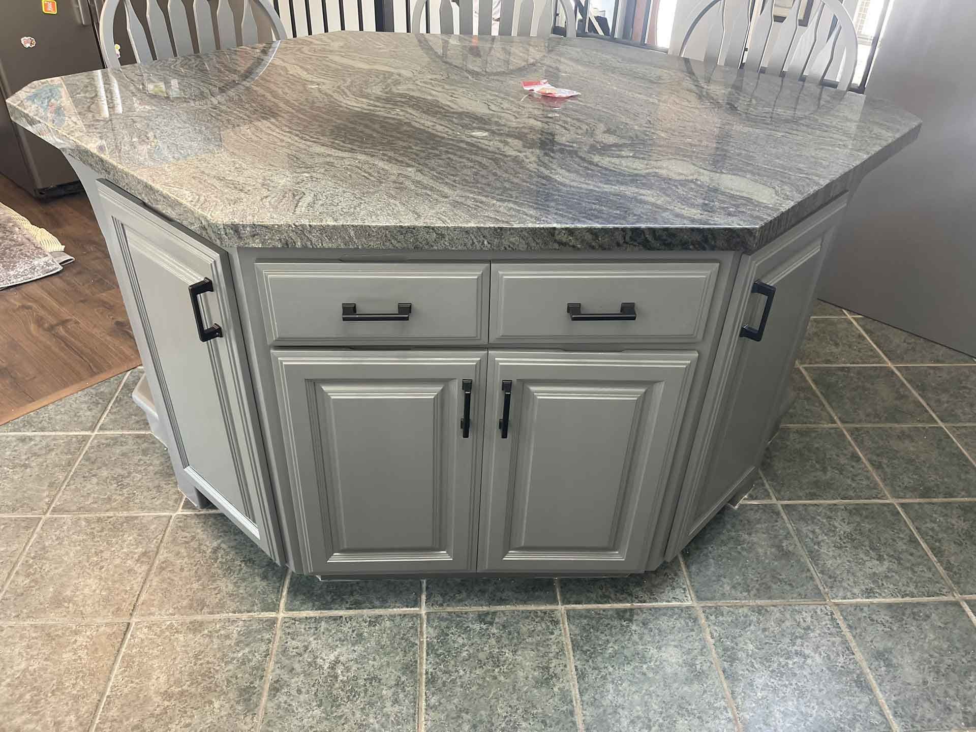 A kitchen island with gray cabinets and a granite counter top.