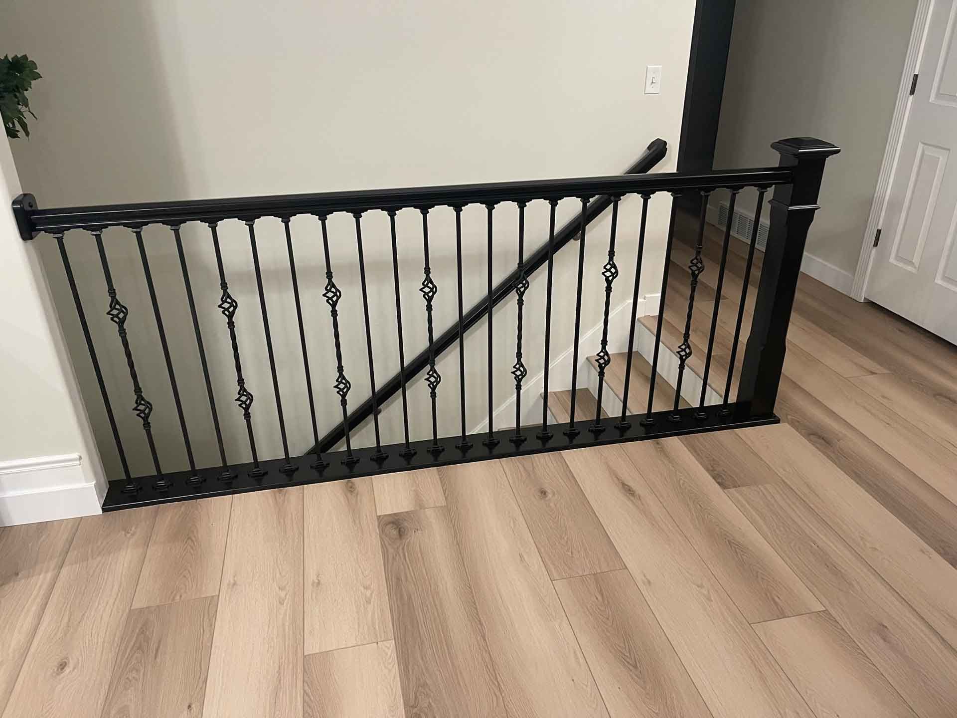 A black railing is sitting on top of a wooden floor next to a staircase.