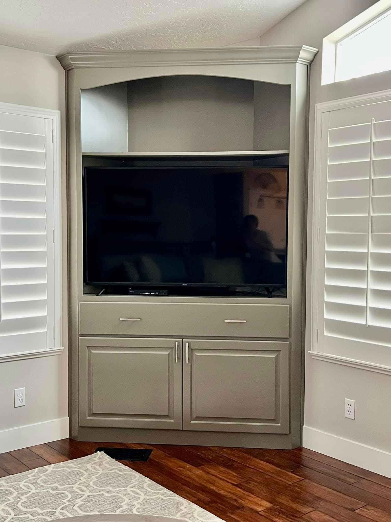 A living room with a corner entertainment center and a flat screen tv.