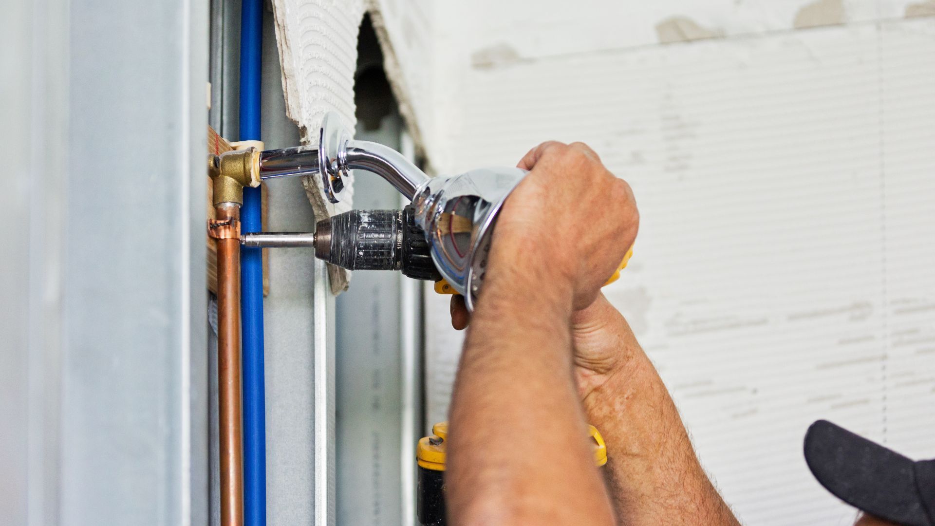 A man is working on a pipe with a drill and wrench.