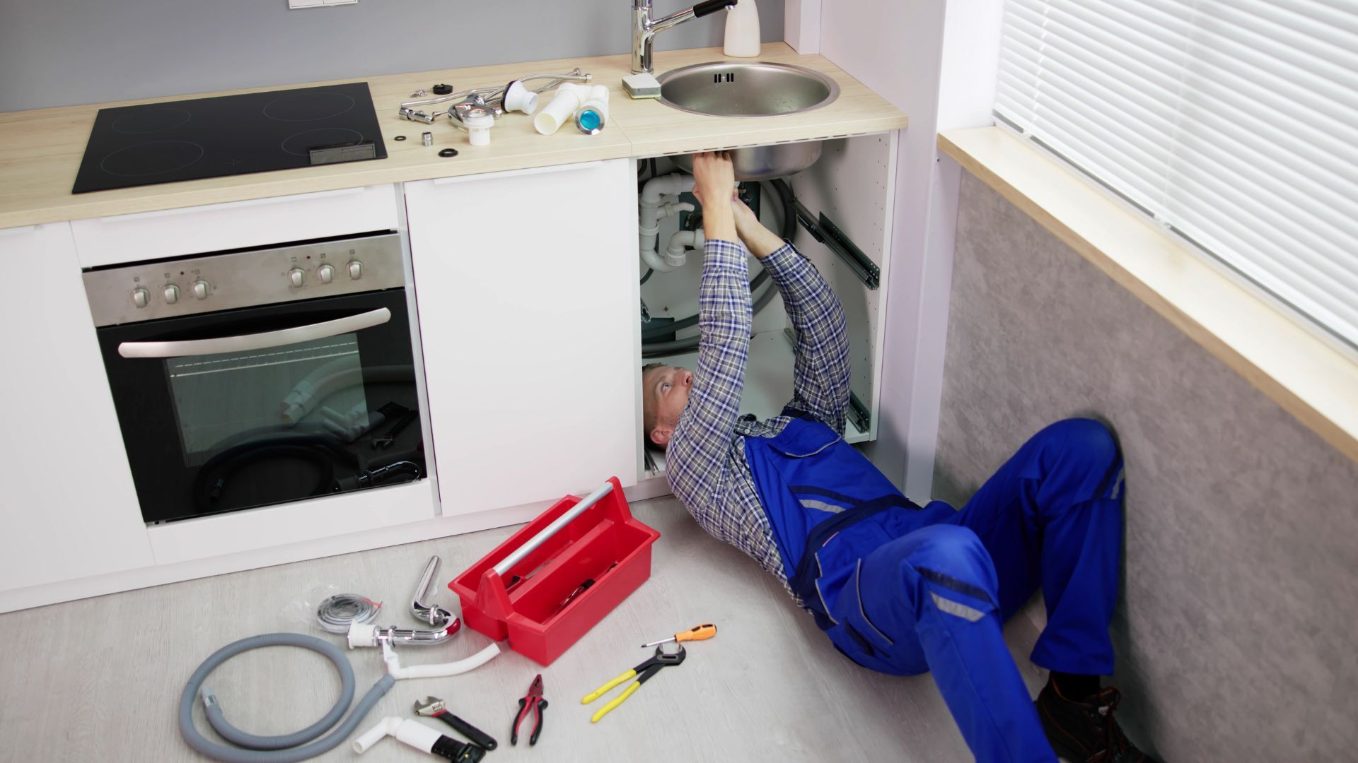 A man is laying on the floor fixing a sink in a kitchen.