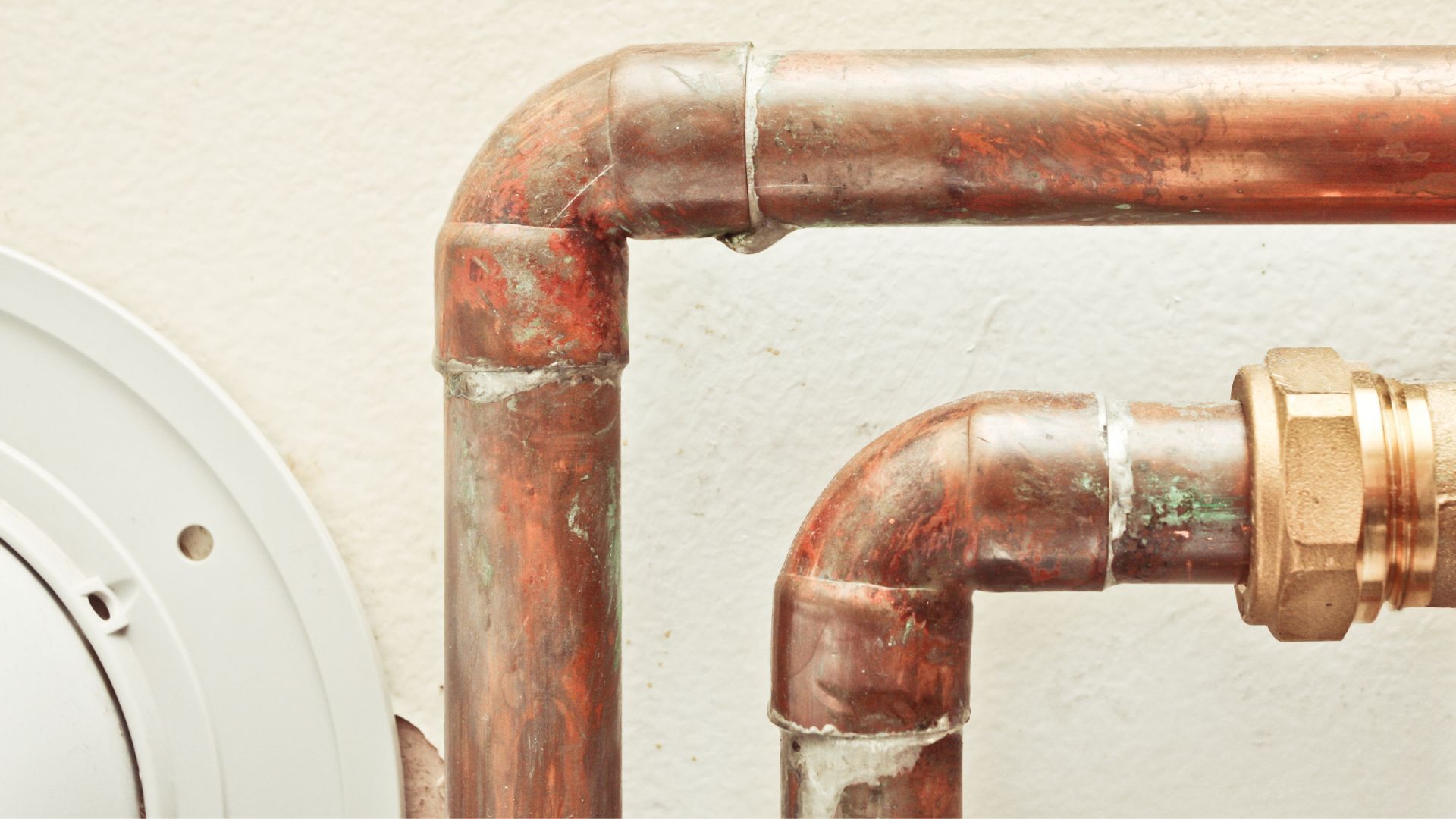 A close up of copper pipes connected to a white wall.