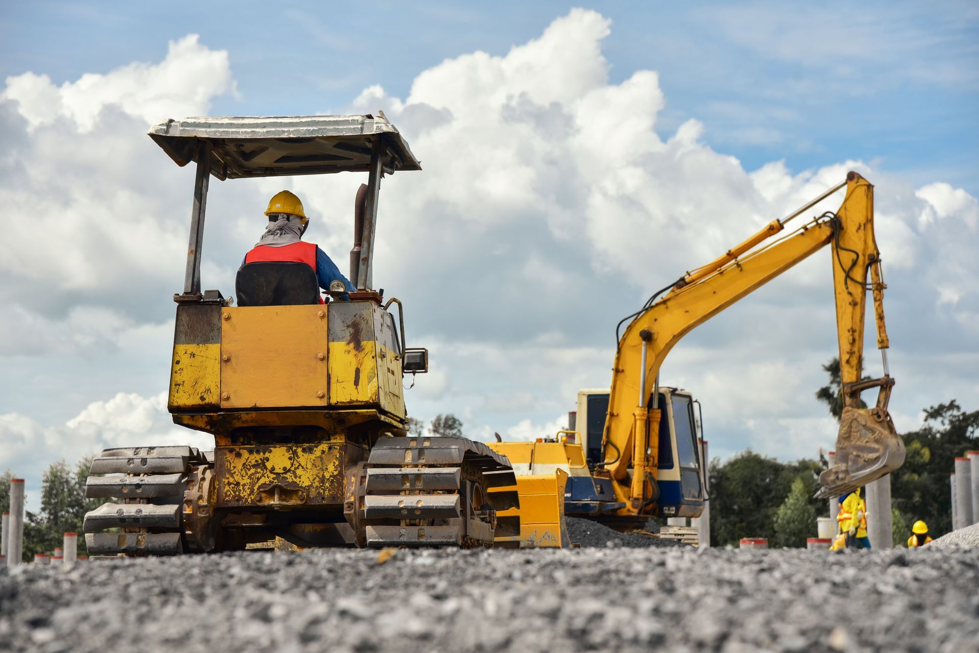 a back view of a man operating a track hoe from with another excavator in the background.