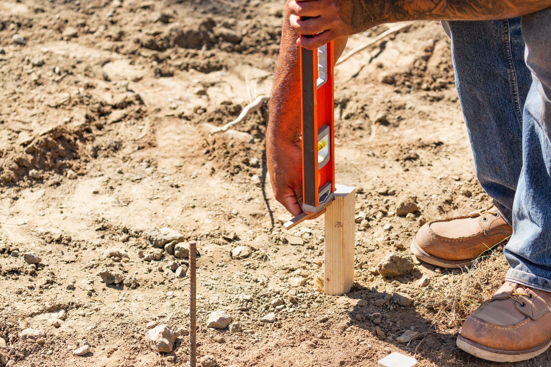 a close up of a man using a small level to lay out a string line for a house footing.