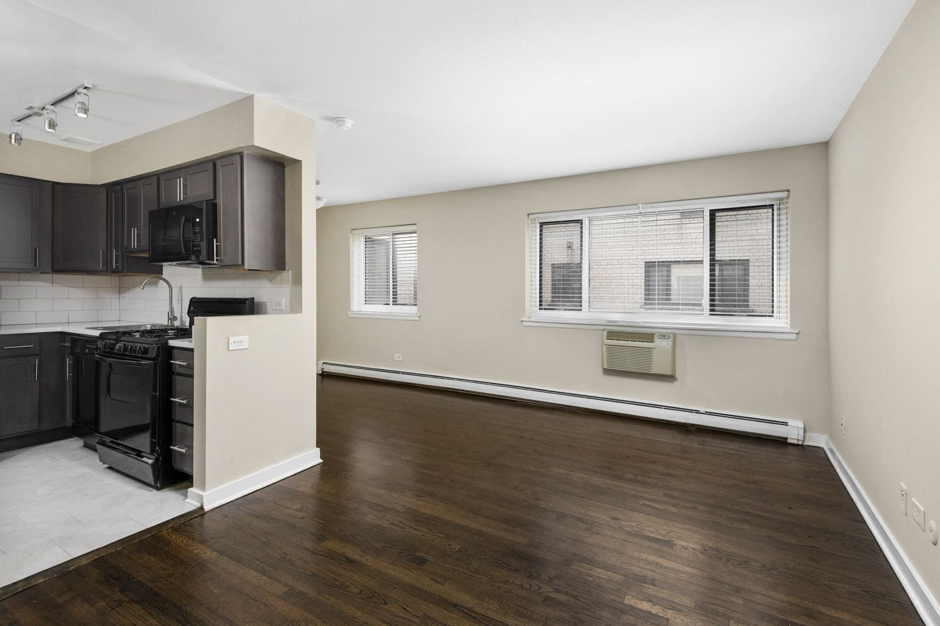 an empty living room and kitchen with wood flooring and black appliances