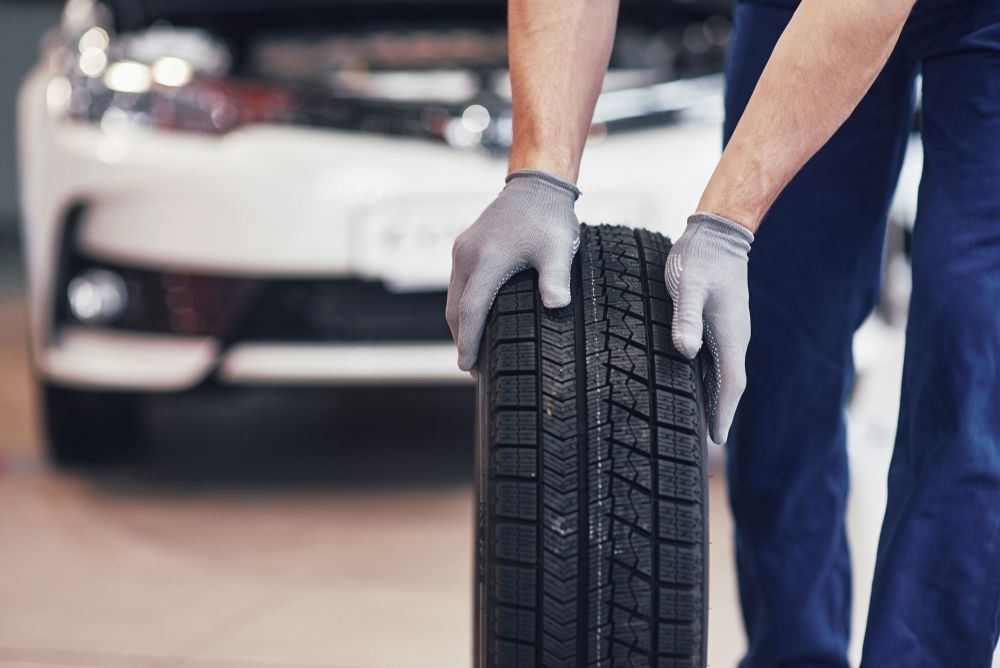 A Man Is Holding A Tire In Front Of A Car — East Lismore Automotive in East Lismore, NSW