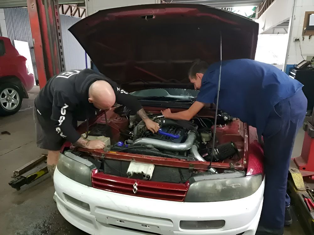 Two men are working on a car bonnet in a workshop — East Lismore Automotive in  East Lismore, NSW
