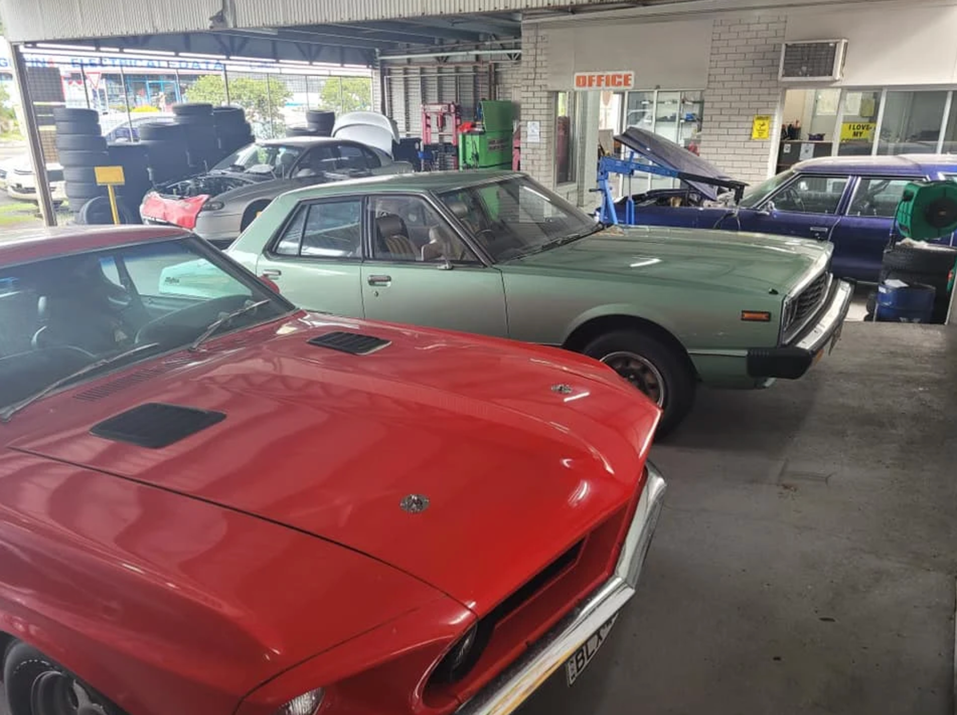 A red and lime green classic cars are parked in a workshop side by side — East Lismore Automotive in East Lismore, NSW