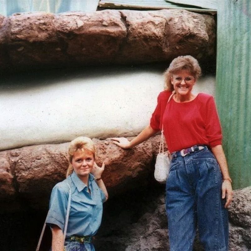 Two women standing next to each other in front of a large rock